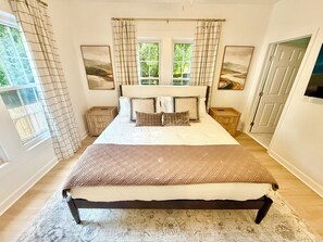 A bedroom with a large bed, two bedside tables, a window with curtains, and artwork on the walls. - Northport Nest- Newly Renovated Modern Farmhouse (Northport)