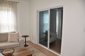 A modern living room with a sofa, a coffee table, a small side table, and a sliding glass door leading to a bedroom. - Northport Nest- Newly Renovated Modern Farmhouse (Northport)