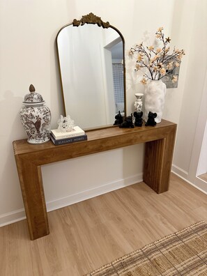 A wooden console table with a mirror, decorative items, and a vase with flowers. - Northport Nest- Newly Renovated Modern Farmhouse (Northport)