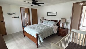 A bedroom with a bed, a nightstand, a ceiling fan, a crib, and two fish wall art pieces. - The River View at Esther’s (Vevay)