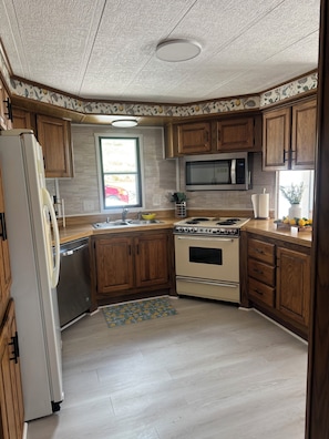 A kitchen with wooden cabinets, a stainless steel refrigerator, a microwave, an oven, and a sink. - The River View at Esther’s (Vevay)
