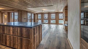A spacious room with a wooden ceiling, large windows, and a central island. - Ski-in/ski-out apartment at Rond-Point des Pistes (Méribel)