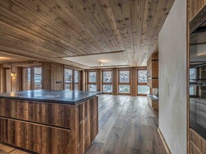 Ein geräumiger Raum mit Holzbalkendecke, großen Fenstern und einer zentralen Insellösung.