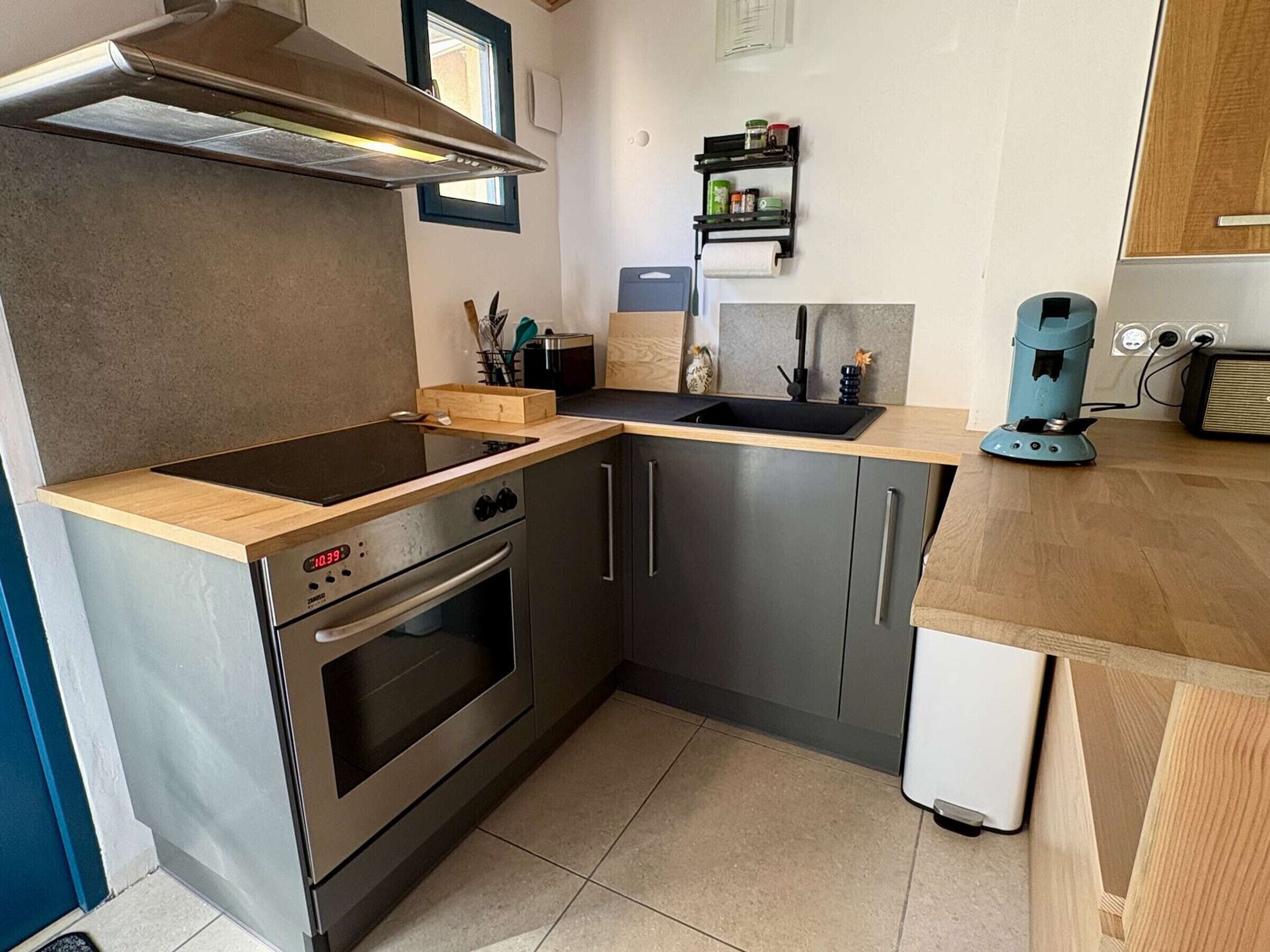 A compact kitchen with a stove, oven, sink, and a small coffee machine.