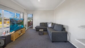 Uma sala de estar com uma grande televisão de tela plana, sofás cinzas, um móvel de entretenimento de madeira e uma vista através de uma porta de vidro.