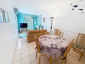A living room with a sofa, TV, and a dining table with chairs. - Apartment sea view - 4 guests (Cabourg)