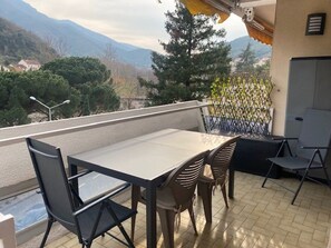 Ein Balkon mit Tisch und Stühlen, Blick auf Berge und eine Umzäunung.