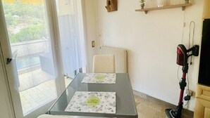 Huoneessa on lasipöytä, tuoli, patteri, hylly, jossa on tavaroita, ja imuri.
