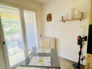 Ein Zimmer mit einem Glastisch, einem Sessel, einem Heizkörper, einem Regal mit Gegenständen und einem Staubsauger.