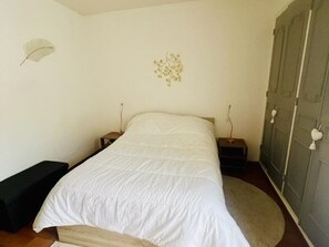 Ein Schlafzimmer mit einem Bett, einem Nachttisch, einer Kommode und einem Wandventilator.