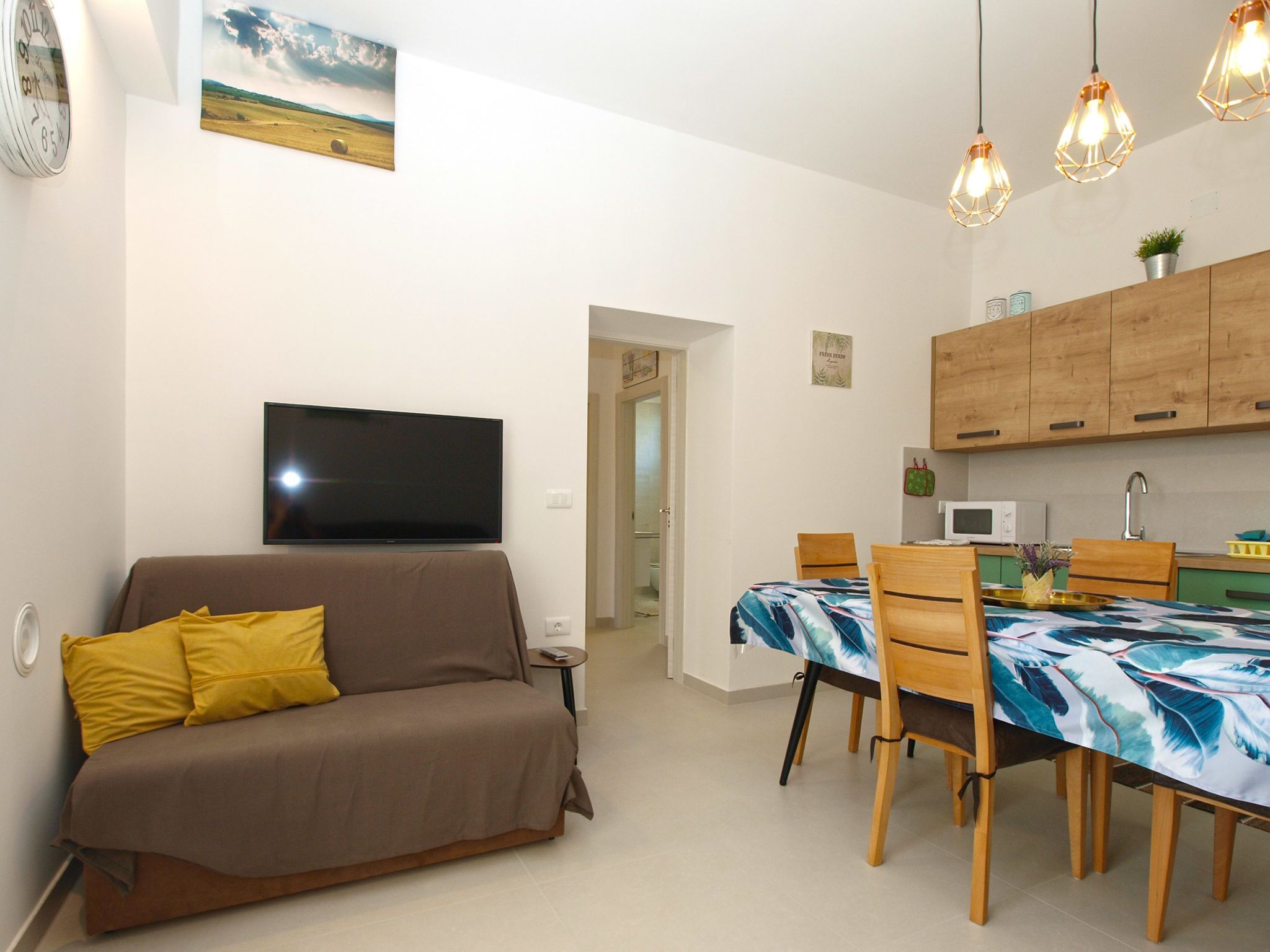 Een woonkamer met een bank, een flatscreen televisie, een eettafel met stoelen en een keuken met houten kastjes.
