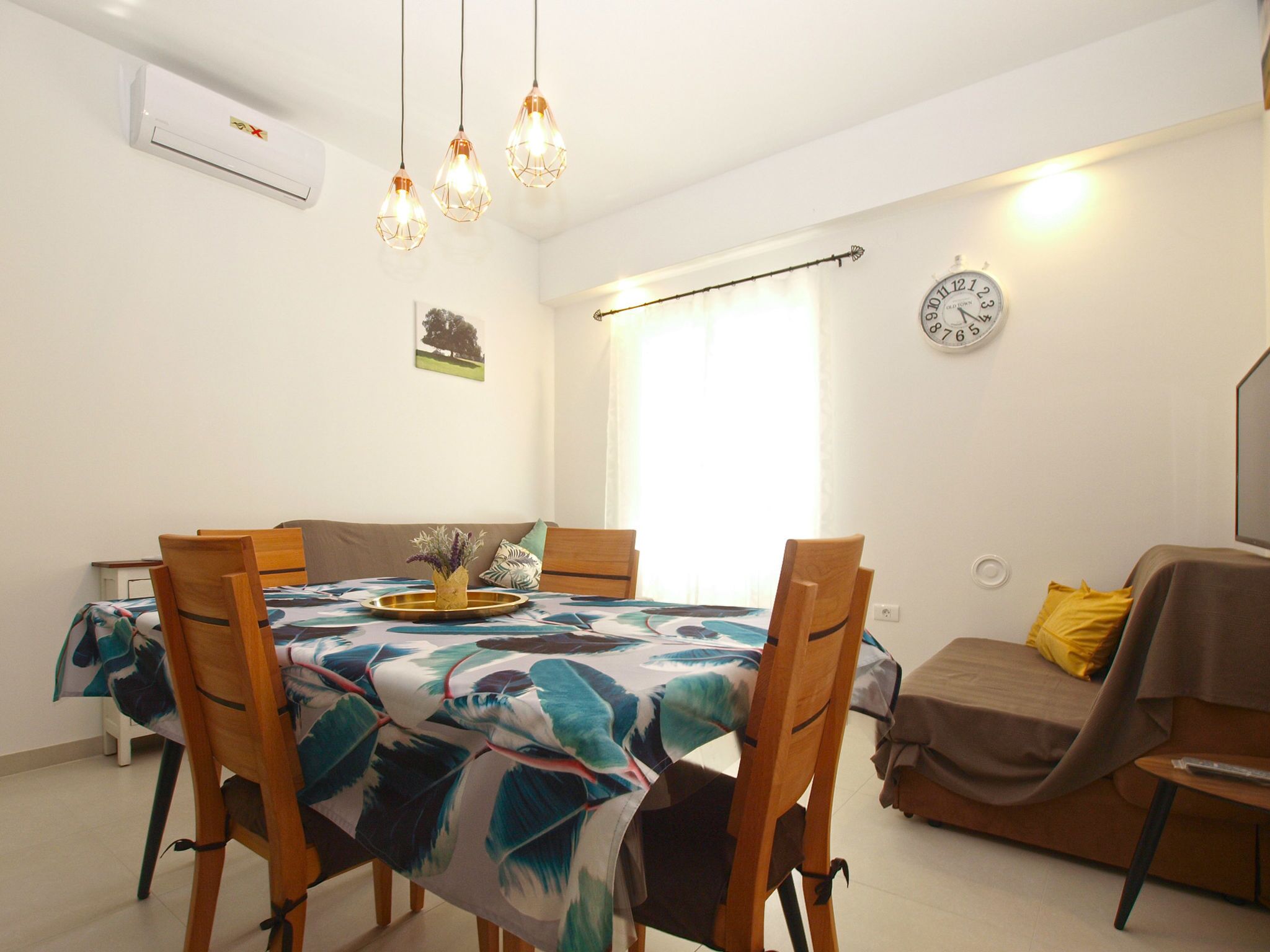 A dining area with a table set for four, a clock on the wall, and a window with curtains.