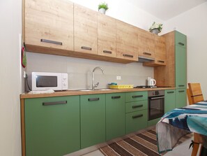 A compact kitchen with wooden upper cabinets, a microwave, a sink, and a stove. - Apartment 1707 by Interhome (Pula/Banjole)