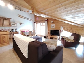 A cozy room with a sofa, a television, a dining table with chairs, and a kitchen area. - Spacious apartment with parking - 6 guests (Crest-Voland)