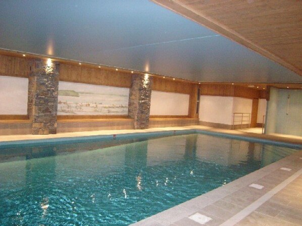 Una piscina interior con pilares de piedra, suelo de baldosas y un mural en la pared.