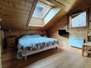A bedroom with a sloped ceiling, a bed, a television, a heater, and a window.