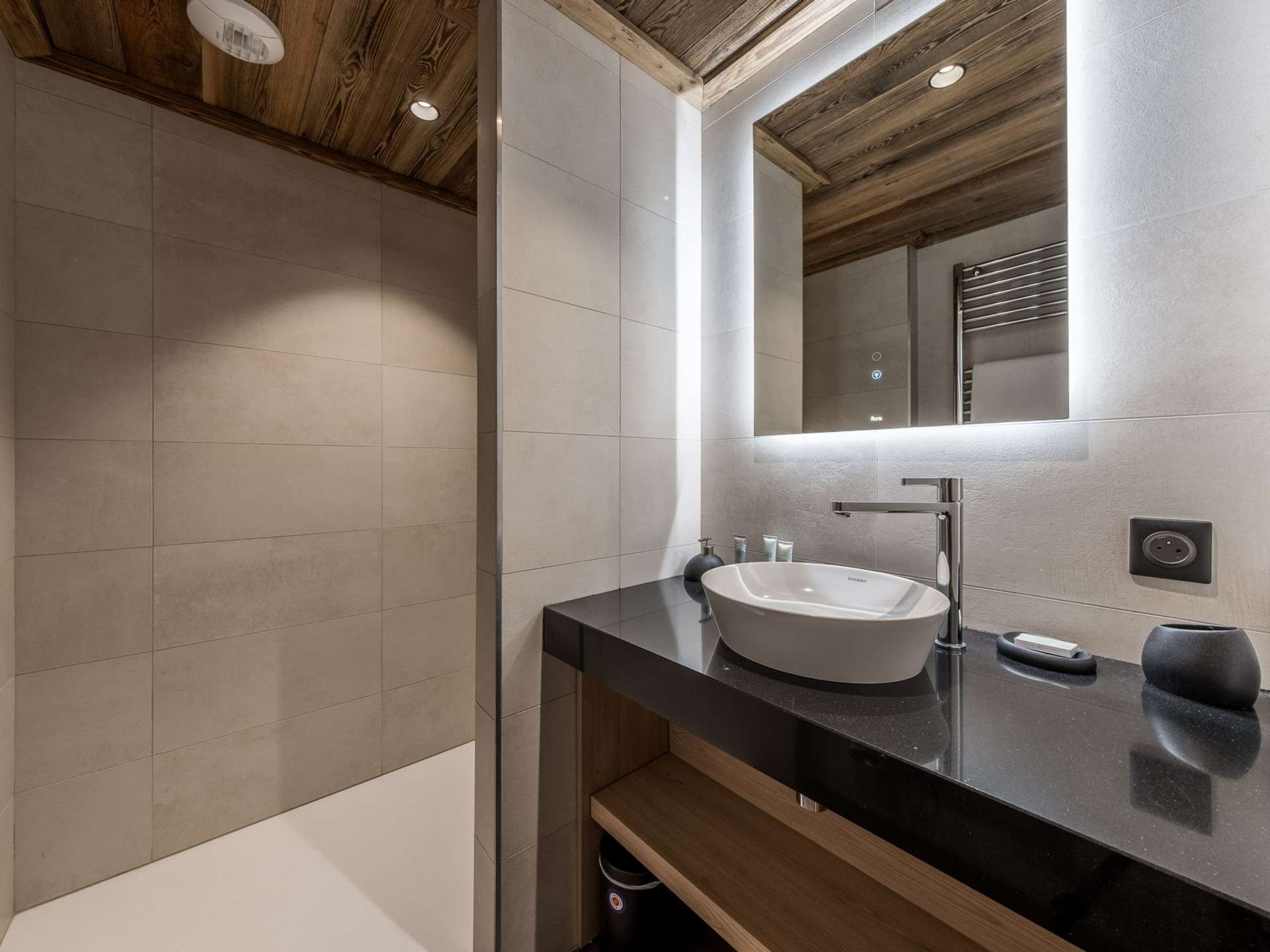 A modern bathroom with a large mirror, a vessel sink, and a wooden ceiling.