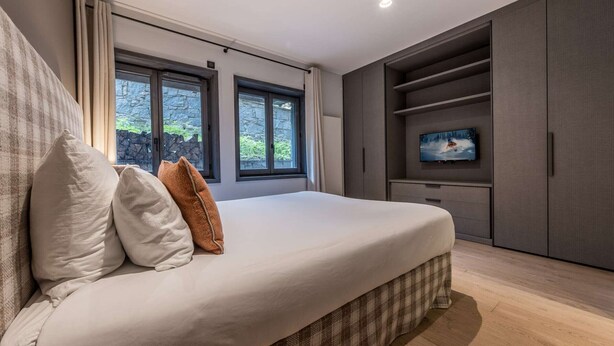 Quarto com cama grande, televisão na parede e vista para o verde lá fora.