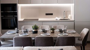 Uma cozinha moderna com eletrodomésticos embutidos, uma área de jantar com mesa de madeira posta para quatro pessoas, e um design minimalista.