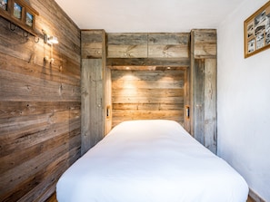 A bedroom with a wooden wall panel design, a bed with white bedding, and a wall-mounted light fixture. - Bright apartment with balcony, Bellevarde view - 4 guests (Val-d'Isère)