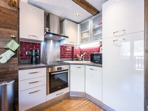 A modern kitchen with white cabinetry, a stainless steel range hood, a Bosch oven, and a red-tiled backsplash. - Bright apartment with balcony, Bellevarde view - 4 guests (Val-d'Isère)