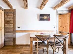 A dining area with a wooden table and chairs, a mounted television, and exposed wooden beams on the ceiling. - Bright apartment with balcony, Bellevarde view - 4 guests (Val-d'Isère)
