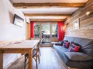A cozy room with a wooden ceiling, a sofa with colorful pillows, a dining table with chairs, and a view of the outdoors. - Bright apartment with balcony, Bellevarde view - 4 guests (Val-d'Isère)