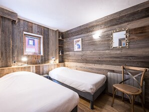 A room with two beds, wooden walls, a radiator, a chair, and a mirror. - Bright apartment with balcony, Bellevarde view - 4 guests (Val-d'Isère)