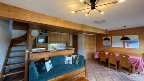 Een gezellig interieur met een houten trap, een bank met kussens, een zithoek met een tafel en stoelen, en een keuken met kastjes en een magnetron.
