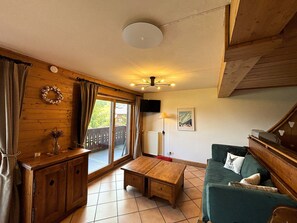 Ein gemütliches Wohnzimmer mit Holzboden, einem grünen Sofa, einem Couchtisch aus Holz und einem großen Fenster mit Vorhängen.