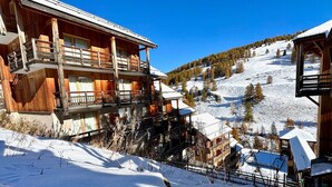 Un chalet de madera con varios balcones, frente a un paisaje montañoso nevado.