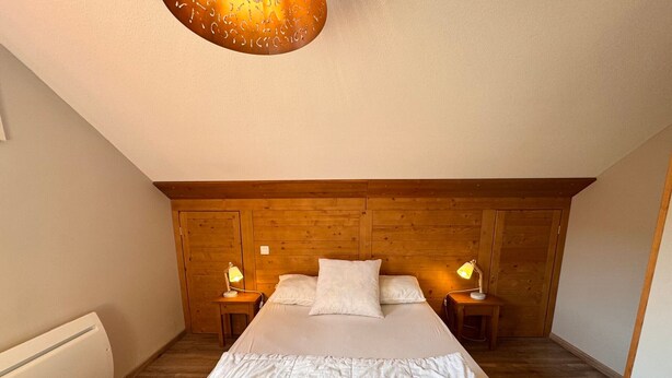 Un dormitorio con cabecera de madera, una cama grande con ropa blanca, dos lámparas de noche y un radiador.