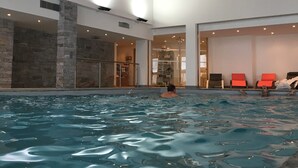 Una piscina interior con agua cristalina, pared de piedra y barandilla de vidrio.