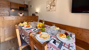 Un comedor con una mesa preparada para cuatro, una cocina al fondo y un televisor de pantalla plana montado en la pared.