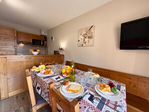 Ein Essbereich mit Tisch für vier Personen, eine Küche im Hintergrund und ein Flachbildfernseher an der Wand.