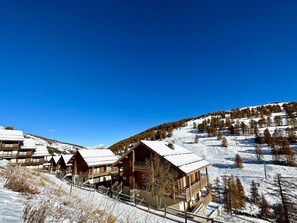 Eine schneebedeckte Lodge mit mehreren Holzhütten, einer Seilbahn und einem Bergpanorama.