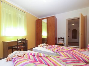 Quarto com duas camas, uma escrivaninha, uma cadeira, um guarda-roupa e uma porta.