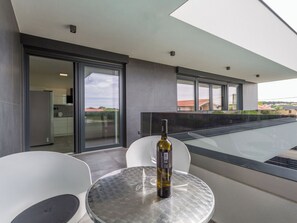A modern outdoor seating area with a glass table and chairs, a bottle of wine, and a view of the cityscape. - House 2258 by Interhome (Pula)