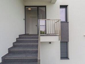 Escada que leva a uma porta, janela com persianas e luminária fixada na parede.