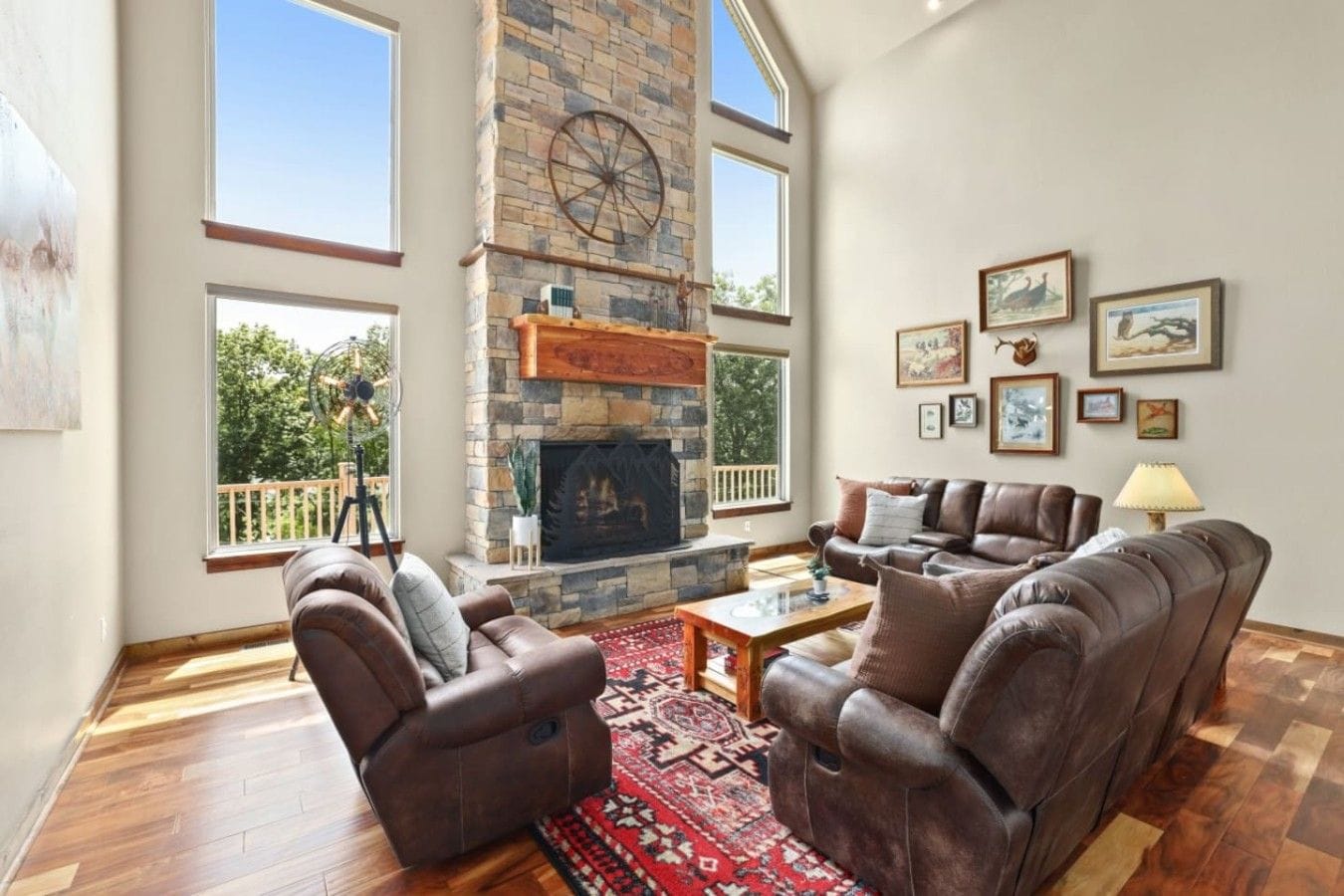 A spacious living room with a stone fireplace, leather sofas, and a large window overlooking greenery.