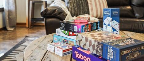 A variety of board games on a wooden coffee table in a living room with a black leather sofa and a patterned rug.