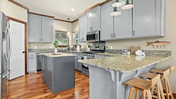 A kitchen with grey cabinets, a granite countertop, stainless steel appliances, and wooden bar stools.