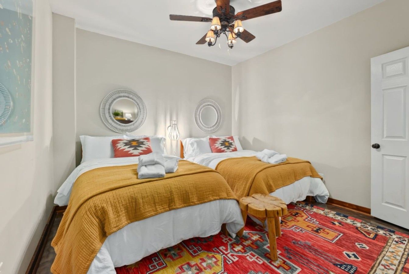 A bedroom with two beds, a ceiling fan, and a patterned rug.