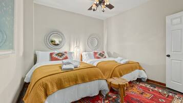 A bedroom with two beds, a ceiling fan, and a patterned rug.
