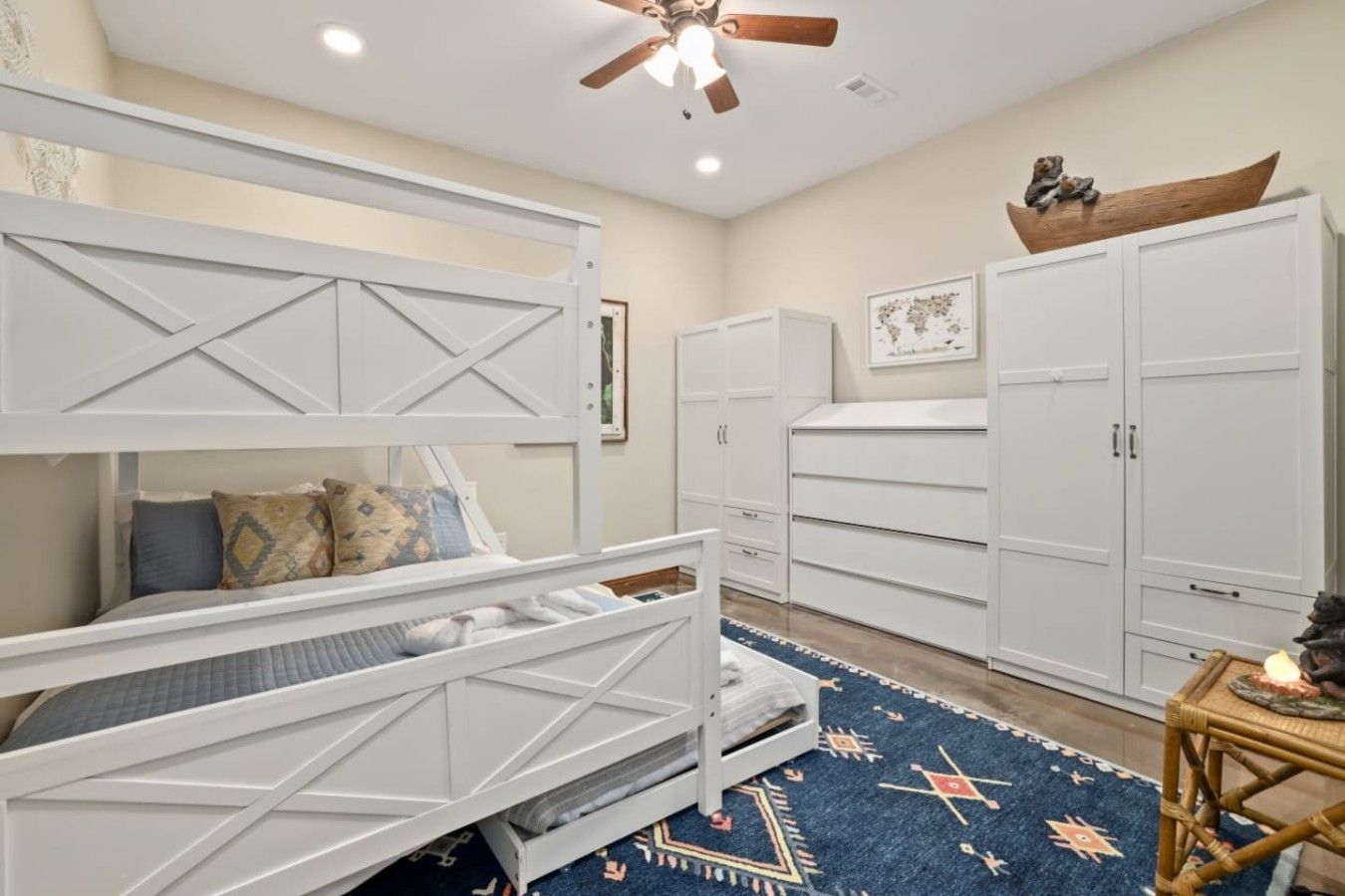 A bedroom with a bunk bed, white cabinets, a ceiling fan, and a patterned rug.