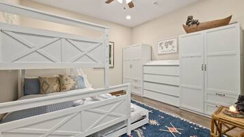 A bedroom with a bunk bed, white cabinets, a ceiling fan, and a patterned rug.