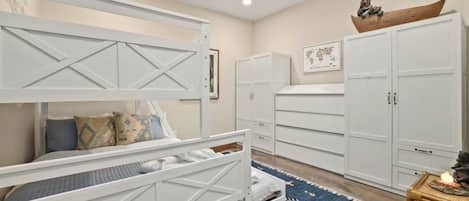 Quarto com cama beliche, armários brancos, ventilador de teto e tapete estampado.