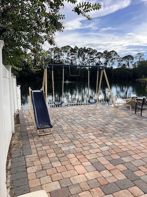 A patio with a swing set, a slide, and a brick pathway leading to a body of water. - Beautiful 3-bedroom townhome with AC in wonderful Jacksonville (Jacksonville)