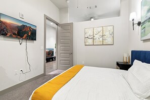 Una camera d'albergo moderna con un letto, una TV a schermo piatto, opere d'arte e una porta che dà su un balcone.