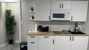 A modern kitchen with white cabinets, a microwave, a sink, and a countertop with a coffee maker and other appliances. - Modern 2BR Retreat | Cozy, Clean & Family-Friendly (Steinbach)